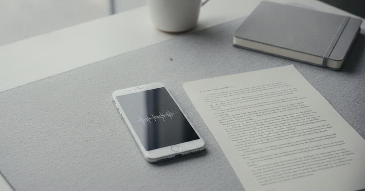 Smartphone showing Voice Memos app waveform beside a printed transcript document on a clean desk, natural light